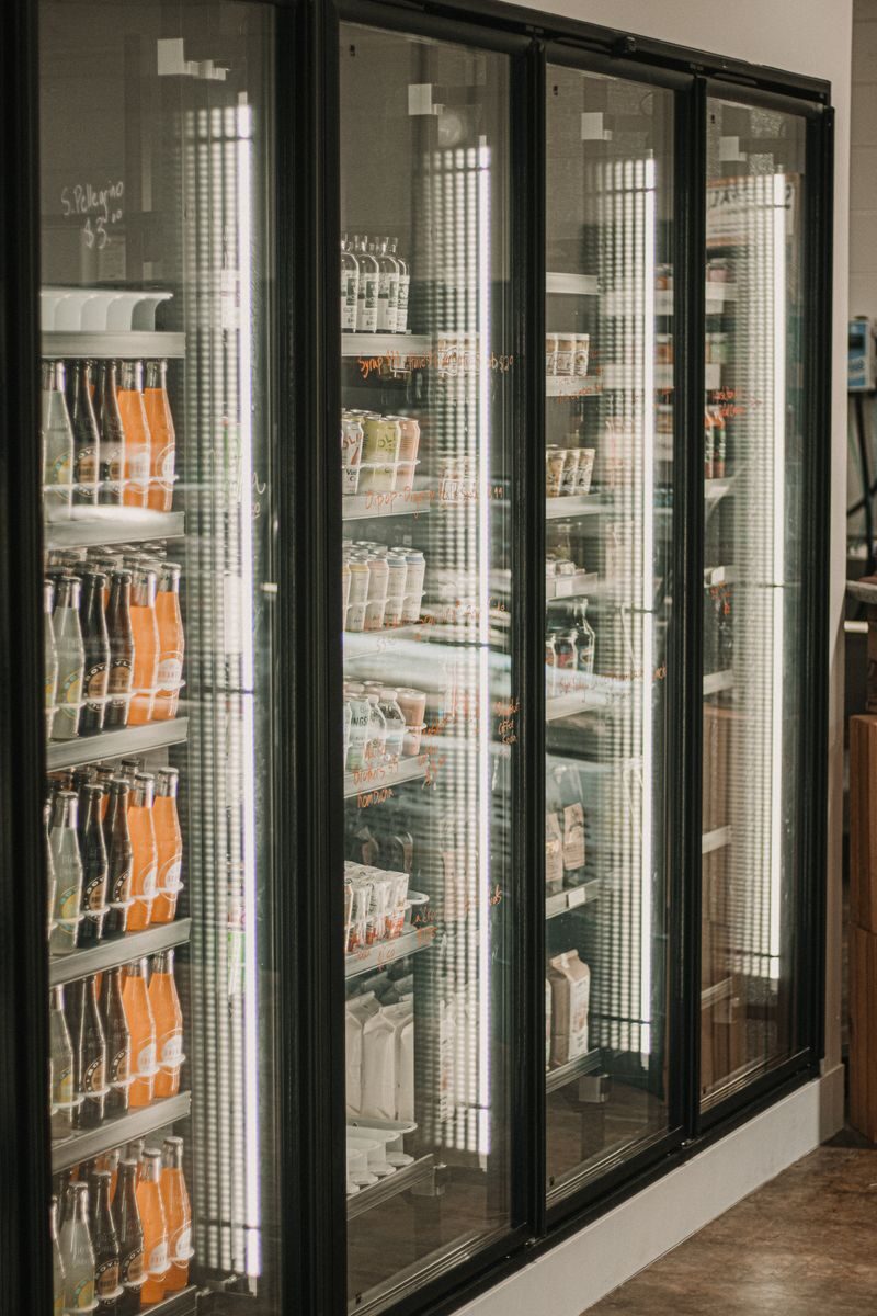 A well-organized beverage and deli section in a grocery store with bright lighting and glass doors.